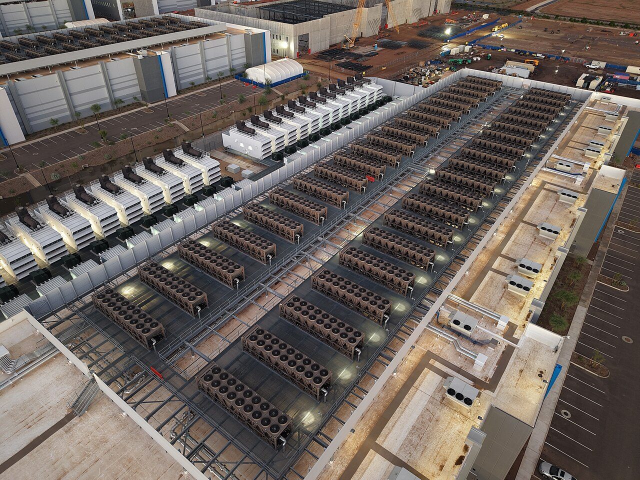 Aerial view of a large data centre roof covered in rows of cooling units with circular fans, with rows of backup generators beside the building