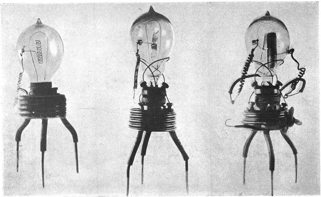 Three early glass vacuum valves standing on wire legs, each a lamp bulb with a filament and an added metal plate or cylinder