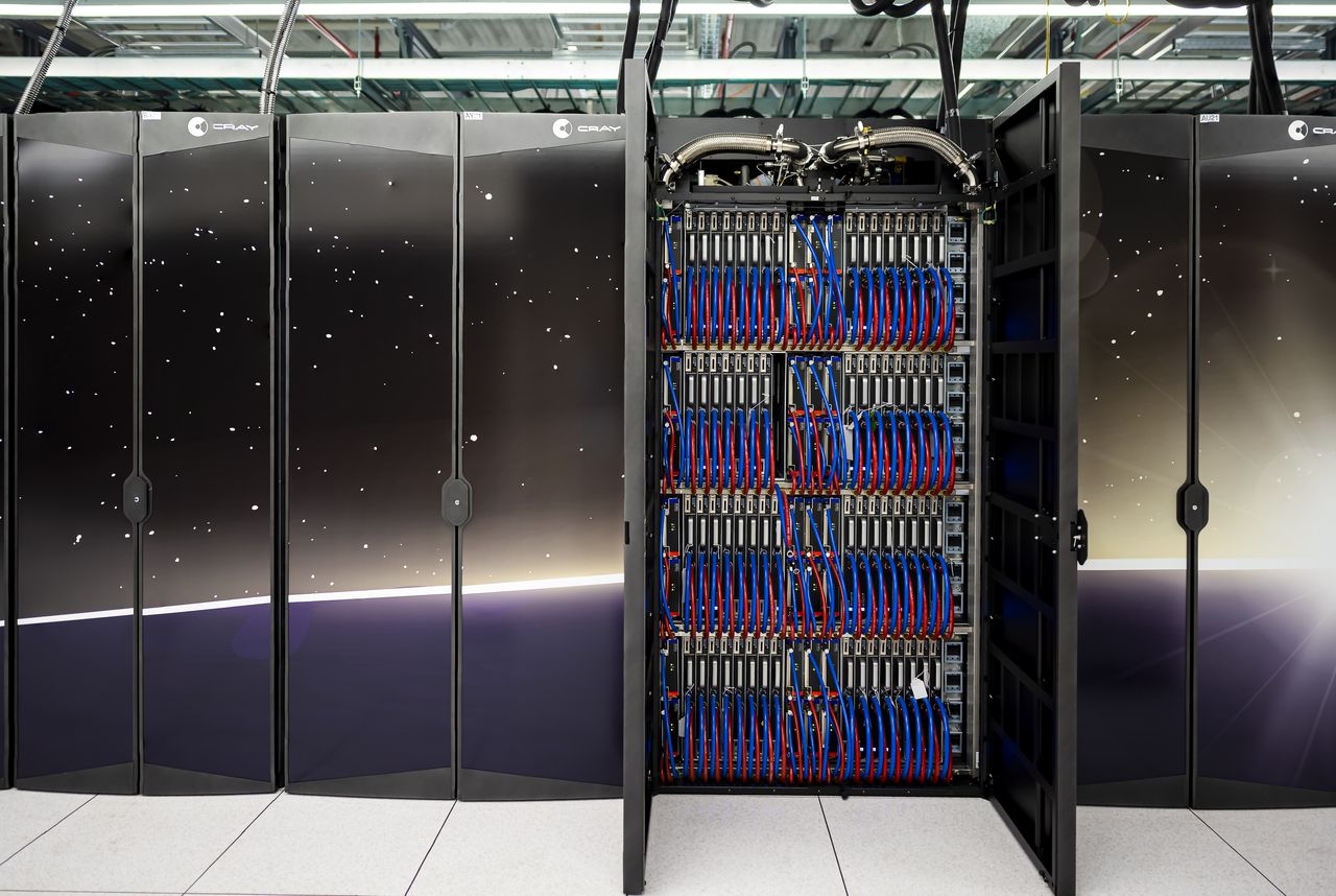 A row of black Frontier supercomputer cabinets decorated with a starfield, one cabinet door open to show four tiers of densely packed compute blades with bundles of blue and red hoses and cables, and silver pipes running along the top