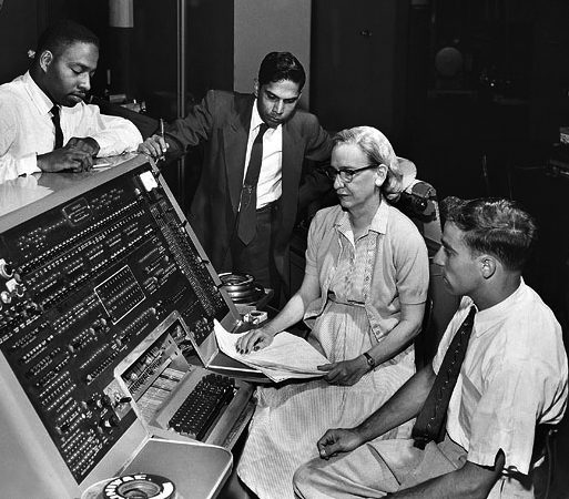 Grace Hopper seated at a UNIVAC console with three colleagues around her in 1957