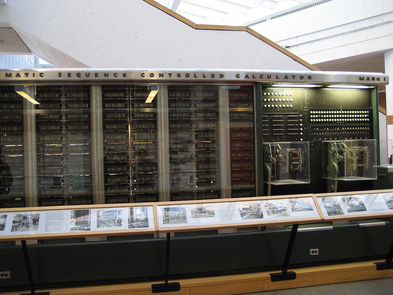 Part of the Harvard Mark I on display: a long wall of glass-fronted cabinets full of relays and counters, under a nameplate reading Automatic Sequence Controlled Calculator
