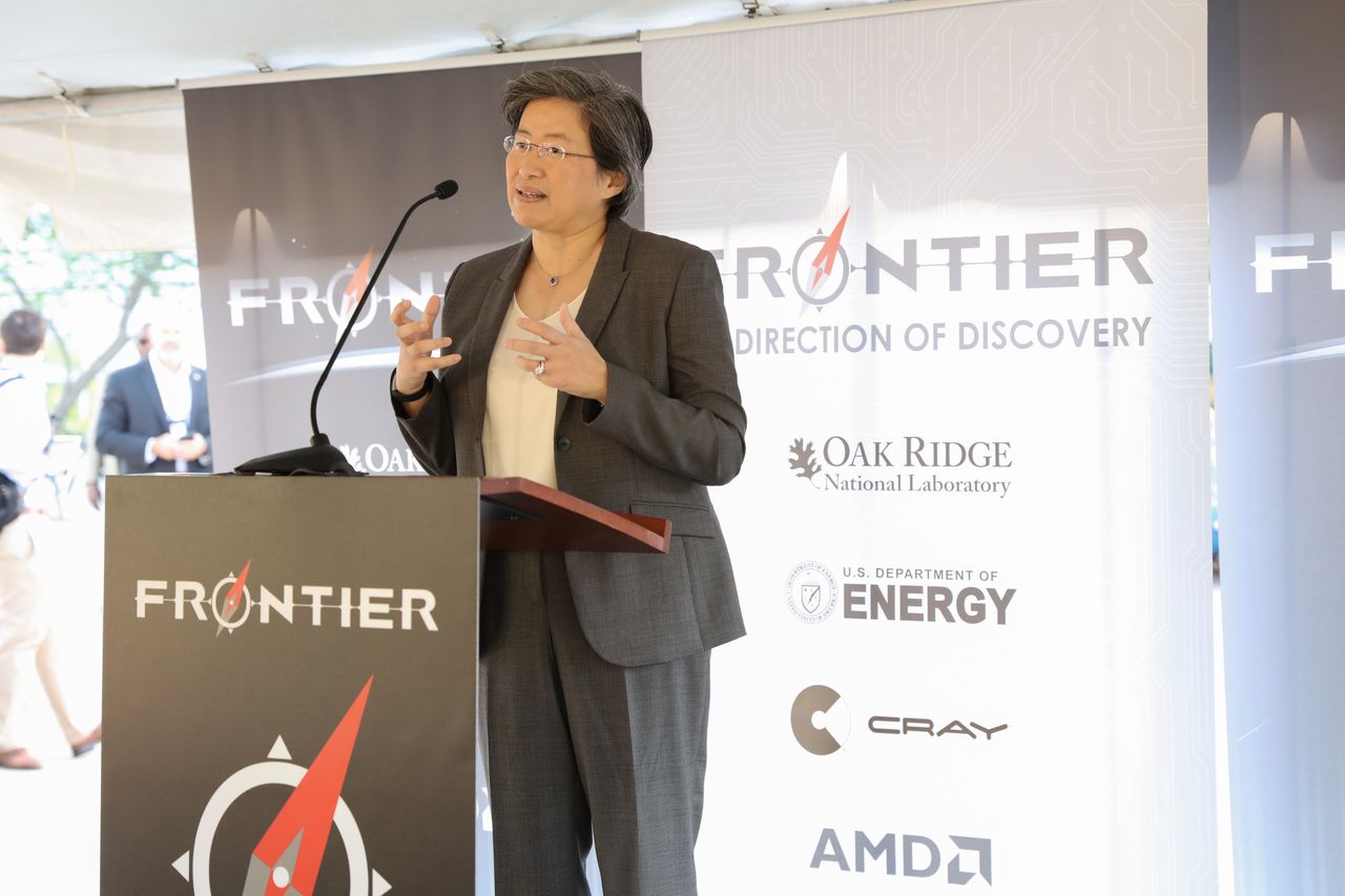 Lisa Su speaking at a lectern under a white tent, with banners behind her reading Frontier, Oak Ridge National Laboratory, US Department of Energy, Cray and AMD