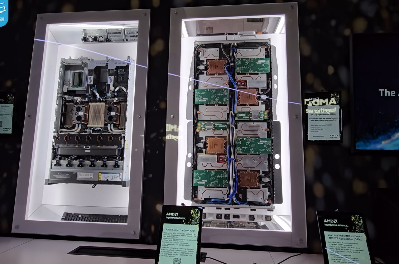 Two servers displayed upright in lit glass cases on a dark exhibition stand: on the left an air-cooled server with large heatsinks, on the right a liquid-cooled sled with copper cold plates, green circuit boards and blue coolant hoses, with AMD information tablets on stands in front