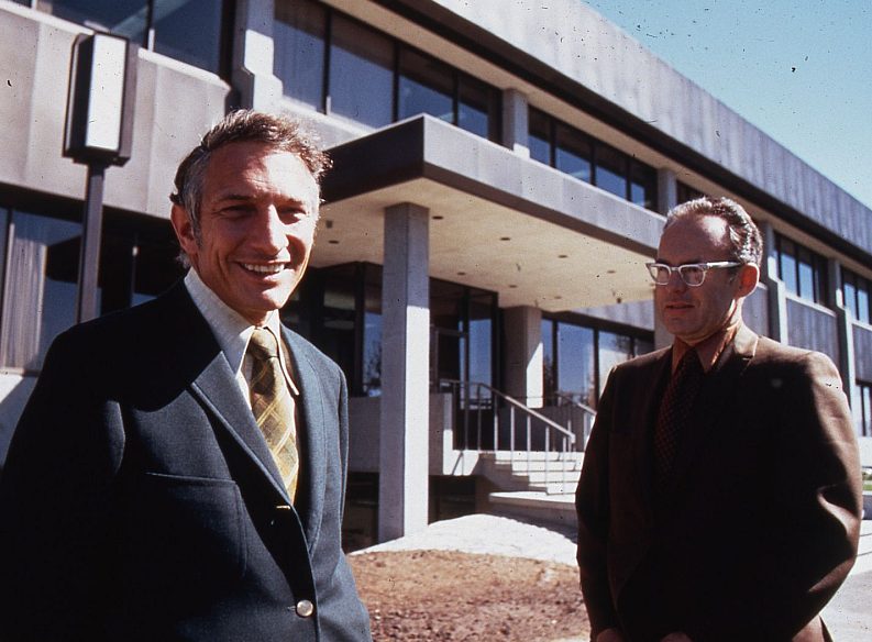 Robert Noyce and Gordon Moore standing outside a modern office building in 1970