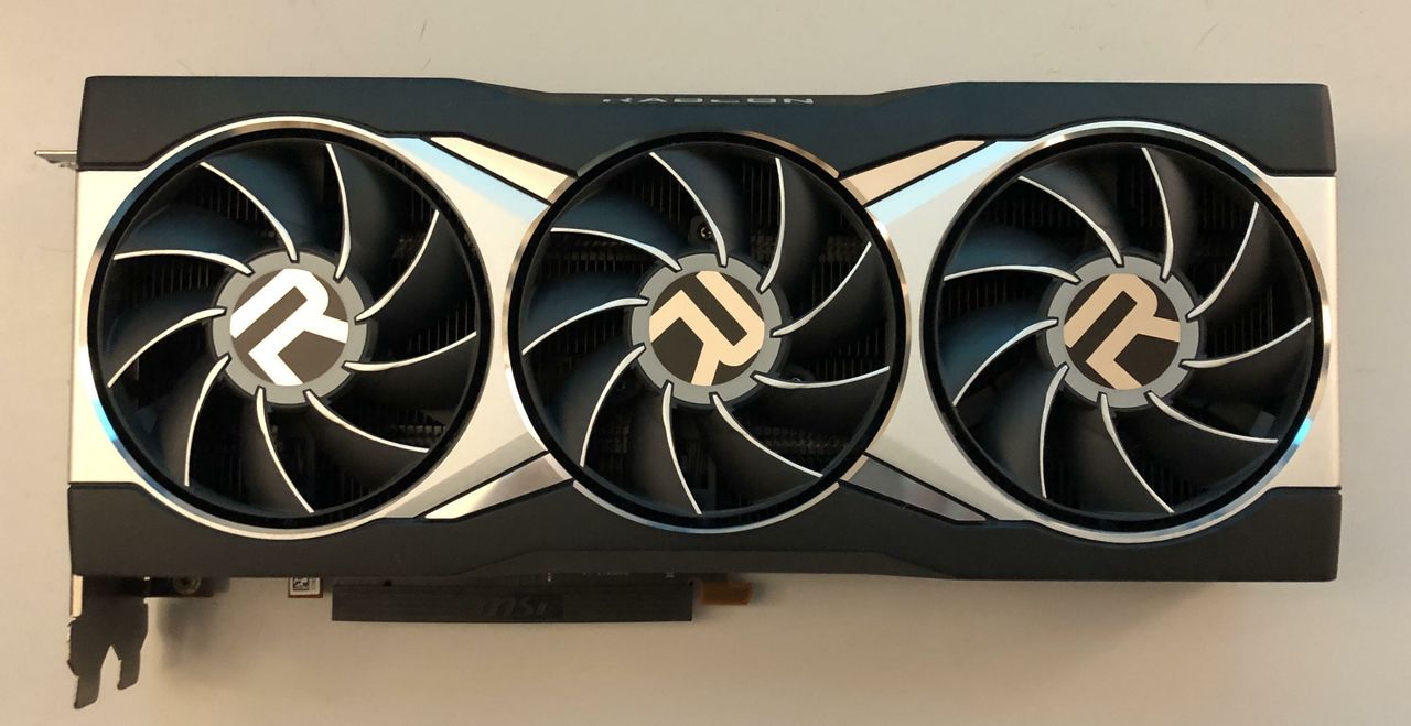 An AMD Radeon RX 6900 XT reference graphics card, a long dark grey card with three black fans each marked with the Radeon R logo and a silver trim along the edge