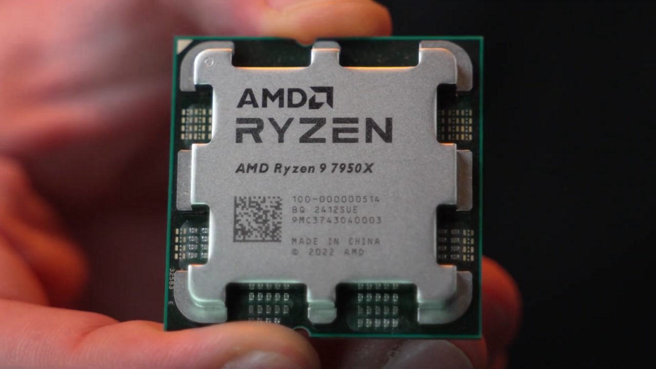 An AMD Ryzen 9 7950X processor held between finger and thumb, showing its silver heat spreader with cut-out edges